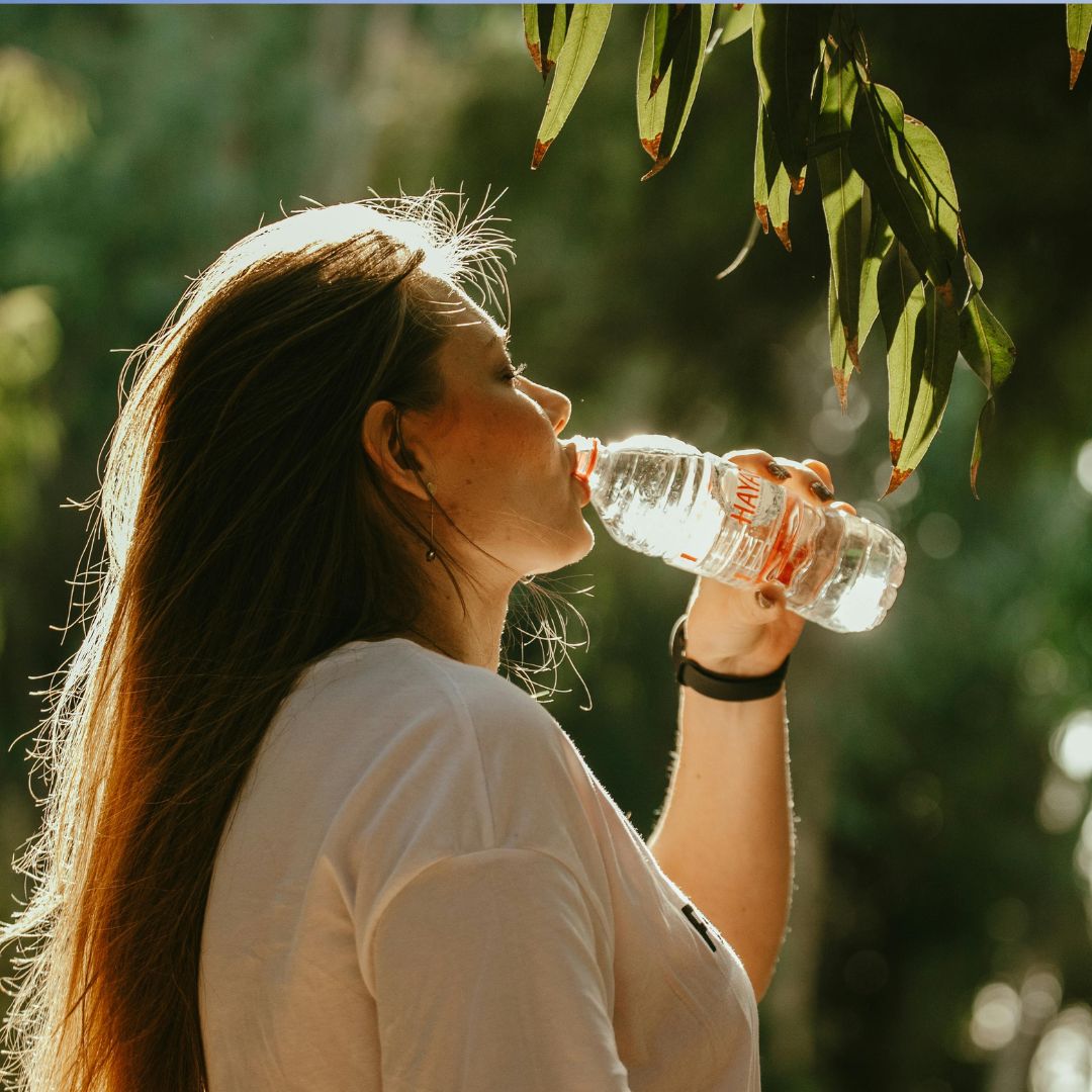 Woman drinking water in summer while travelling, with light clothing and healthy snacks for PMOS support.